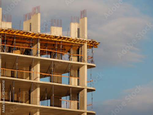 Image of a multi-story building under construction with concrete columns and metal scaffolding, taken from a low angle in late afternoon