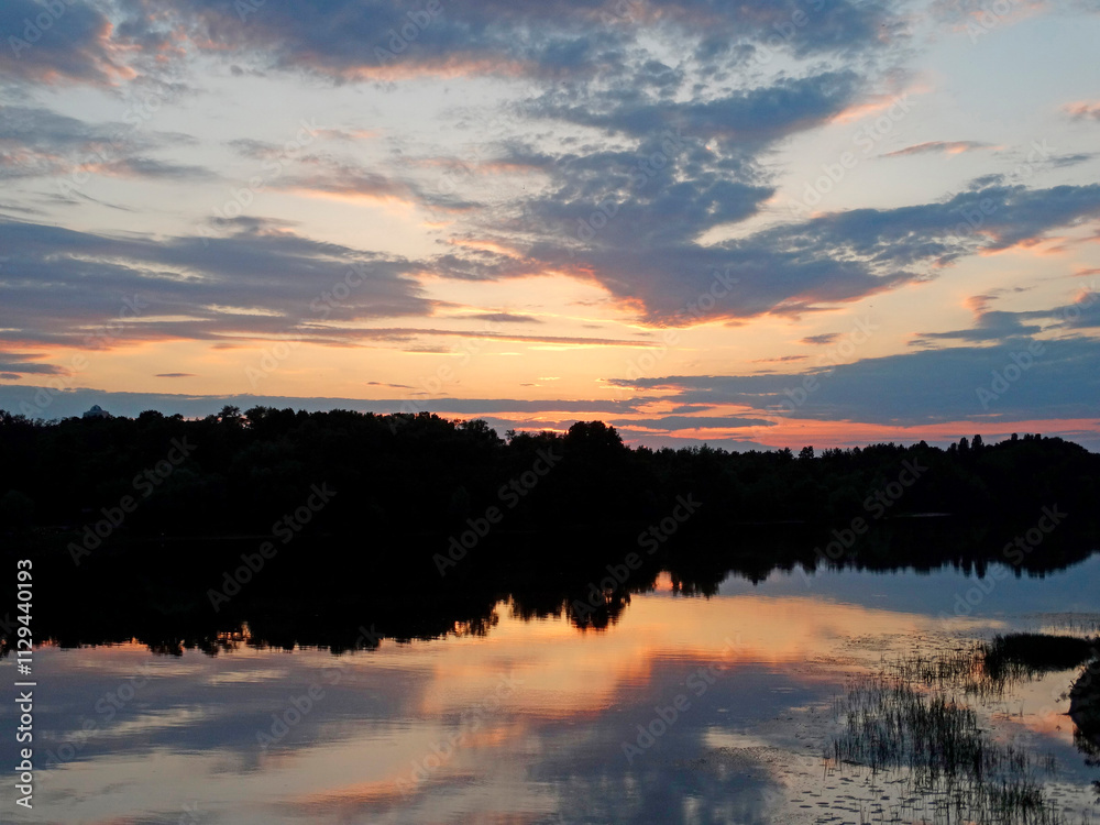 A tranquil sunset scene over a lake, with trees flanking the sides The vibrant sky, reflecting on the calm water, creates a mirror effect A tranquil sunset scene over a lake, with trees flanking the sides The vibrant sky, reflecting on the calm water, creates a mirror effect