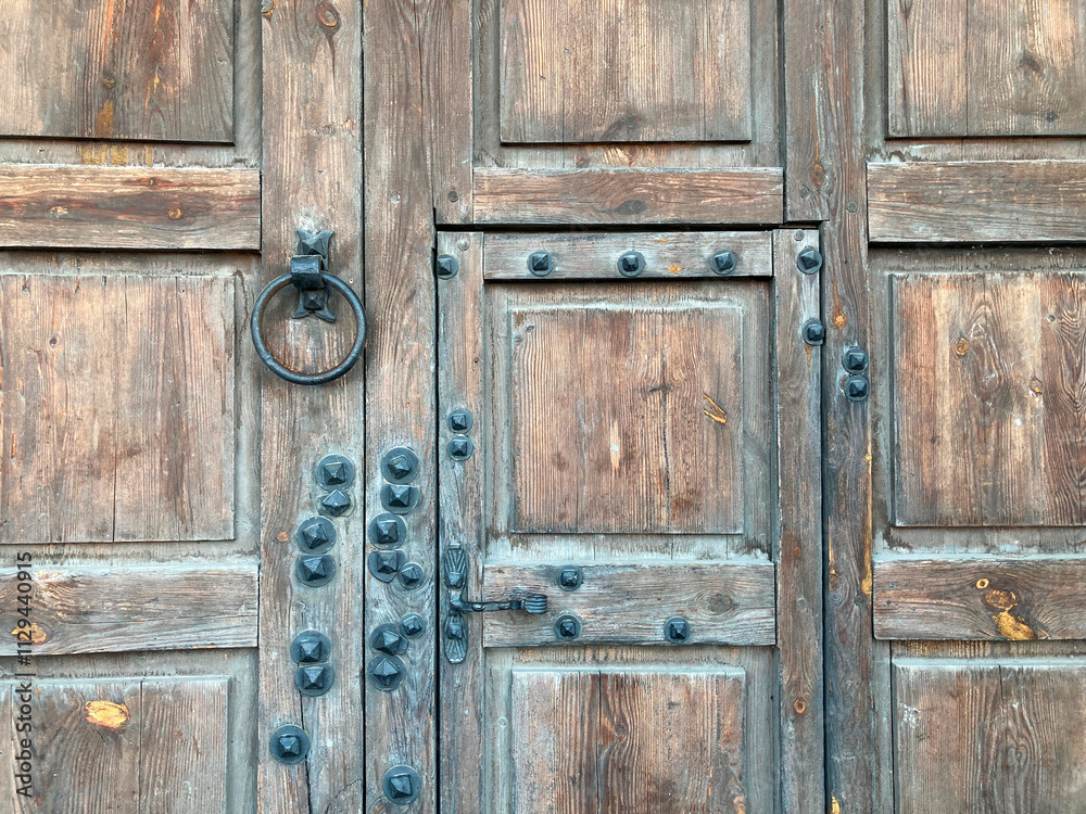 An old, weathered wooden door with metal hardware and visible locksbolts is depicted The background suggests a larger structure within the same building complex An old, weathered wooden door with metal hardware and visible locksbolts is depicted The background suggests a larger structure within the same building complex