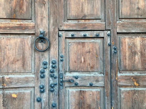 An old, weathered wooden door with metal hardware and visible locksbolts is depicted The background suggests a larger structure within the same building complex