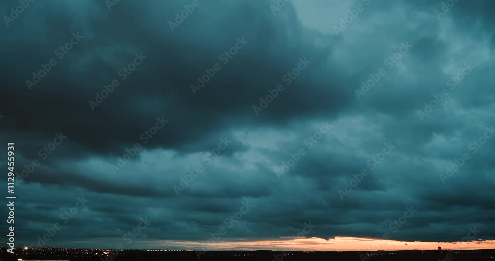 Timelapse of a wide angle view of the sky with fast moving dark blue clouds turning darker and getting an orange tint by city lights and of the horizon lit by sunset and lights of traffic on a highway