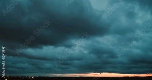 Timelapse of a wide angle view of the sky with fast moving dark blue clouds turning darker and getting an orange tint by city lights and of the horizon lit by sunset and lights of traffic on a highway