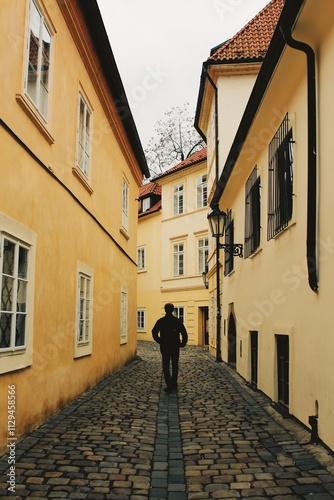Black Silhouette of a Man Walking Down a Cobblestone Street Surrounded by Yellow Buildings in Prague