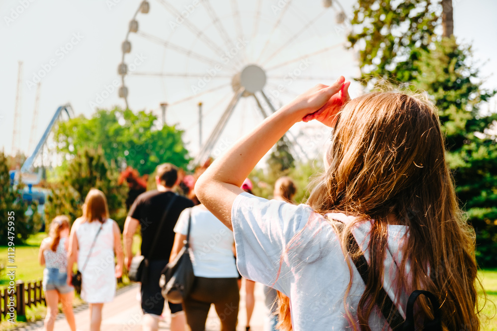 Obraz premium A young girl in an amusement park with a Ferris wheel in the background.