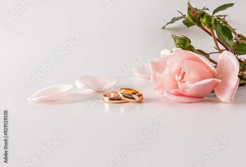 Elegant wedding rings with pink rose and petals on white background photo