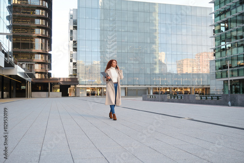 Confident woman walking in urban setting holding laptop