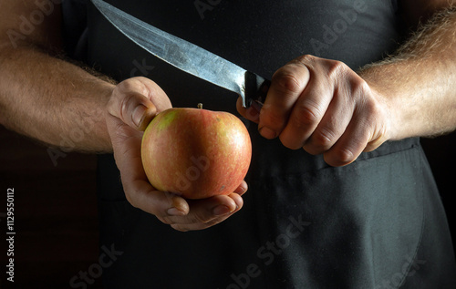 A pair of hands hold a vibrant apple while a knife hovers above it, poised for cutting. Soft light filters into the kitchen, creating a warm and inviting atmosphere for culinary creativity photo