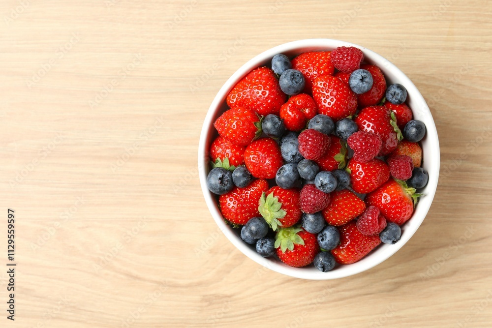 Different fresh ripe berries in bowl on wooden table, top view
