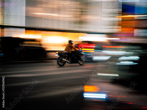 Motorcycle with rider in helmet riding through bright Tokyo city lights at night quickly. Speeding or in a rush amongst traffic and urban buildings with vibrant colours and panning motion blur