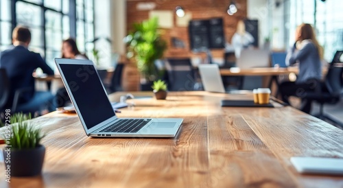 Table en bois avec ordinateurs portables sur un arrière-plan flou de gens travaillant dans un bureau d'entreprise.