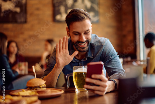 Happy man making video call via cell phone in pub.