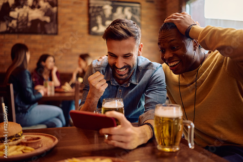 Cheerful men celebrating while using sports app on smart phone in bar.