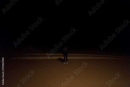 Solitary Figure in the Night: A lone person stands silhouetted against an overwhelmingly dark background, creating a mood of mystery and contemplation. The image evokes feelings of isolation. photo