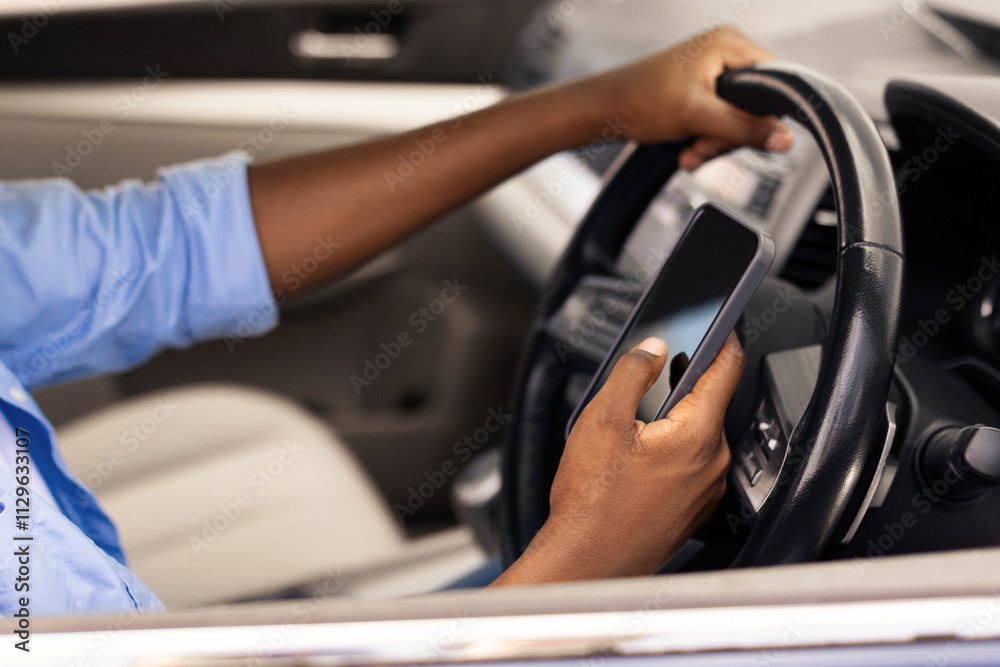 Naklejka premium Positive black male driver holding mobile phone while driving nice auto, using new mobile application for navigation going on vacation or making summer trip, stuck in traffic jam, profile side view