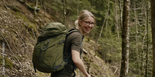 Young blonde woman with glasses hiking in the forest with a large backpack, enjoying the fresh air and lush greenery