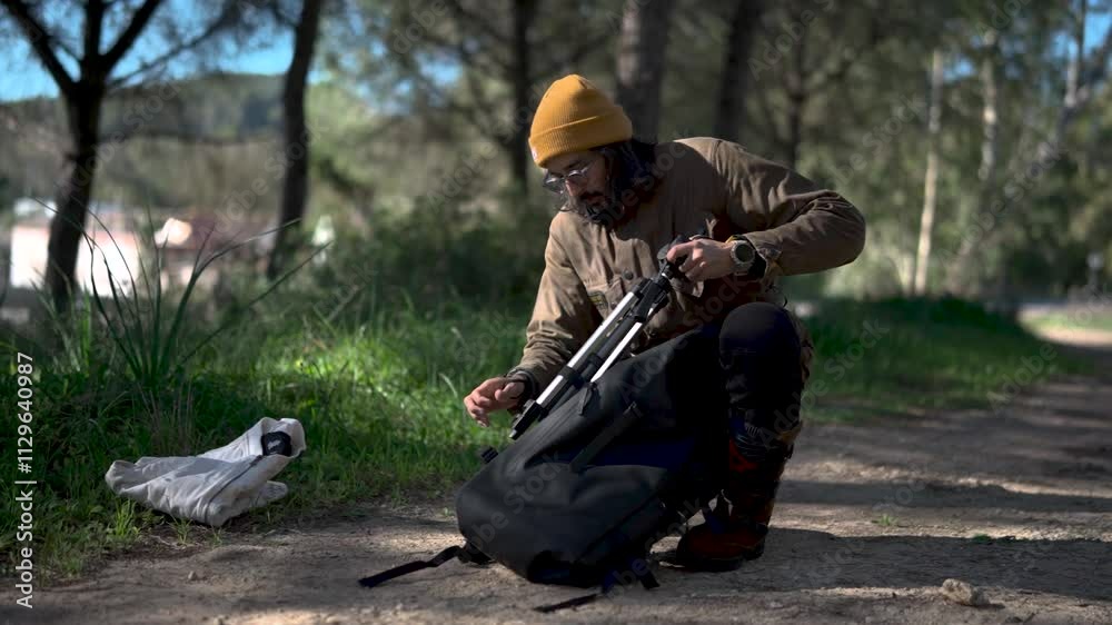 Hombre joven con barba sacando tripode para crear contenido en el bosque