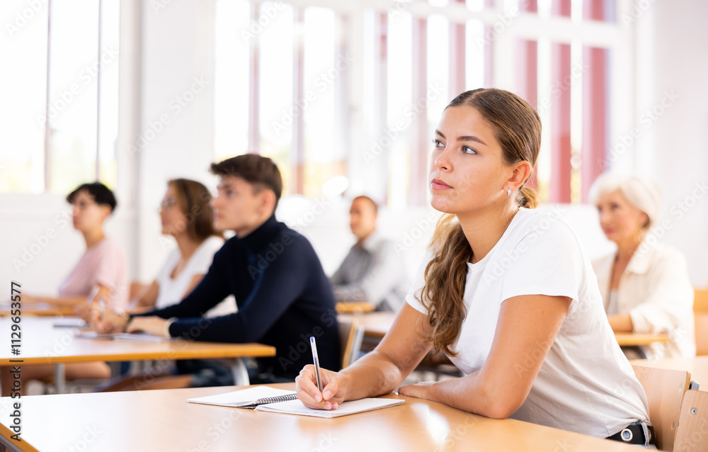 Portrait of focused young attractive girl attending lecture as part of graduate education with mixed age group Portrait of focused young attractive girl attending lecture as part of graduate education with mixed age group