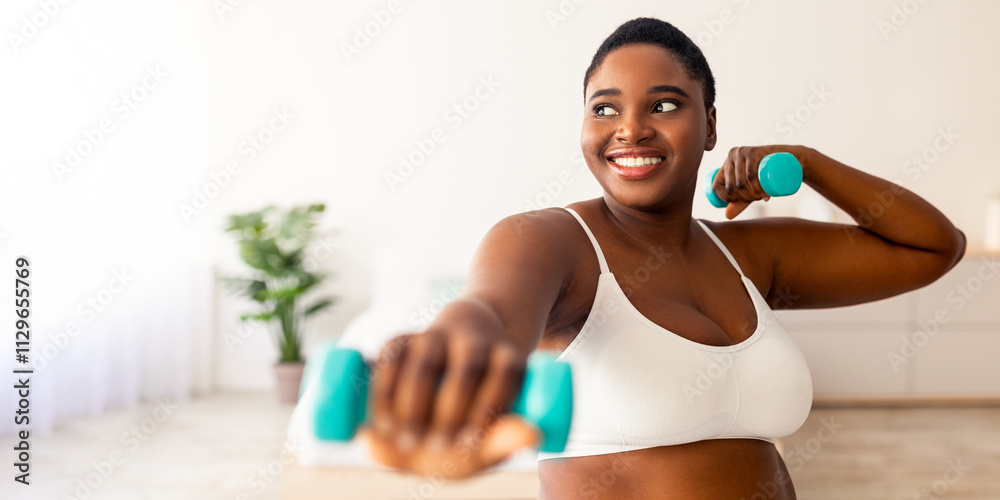 Home sports for weight loss. Happy plus size black woman doing fitness exercises with dumbbells indoors. Millennial overweight lady strengthening her biceps, leading active lifestyle Home sports for weight loss. Happy plus size black woman doing fitness exercises with dumbbells indoors. Millennial overweight lady strengthening her biceps, leading active lifestyle