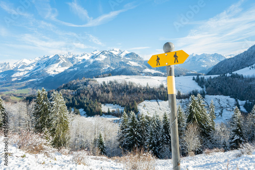 Swiss alpine landscape panorama in the winter wonderland of Switzerland in the snow with a hiking trail sign giving directions