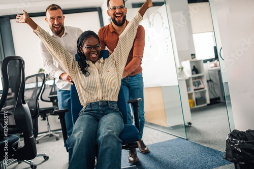 Business colleagues pushing businesswoman on office chair, having fun at work photo