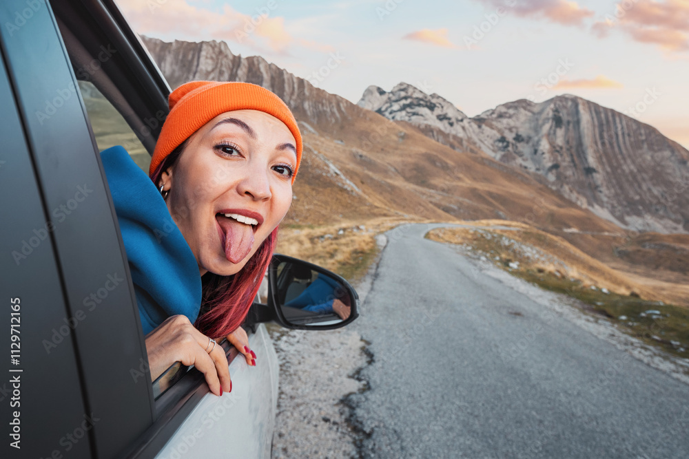 Carefree tourist enjoying road trip, sticking tongue out of car window in mountain landscape