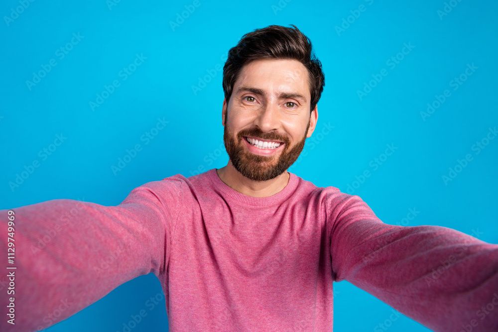 Cheerful man with a beard taking a selfie against a bright blue backdrop in casual fashion Cheerful man with a beard taking a selfie against a bright blue backdrop in casual fashion