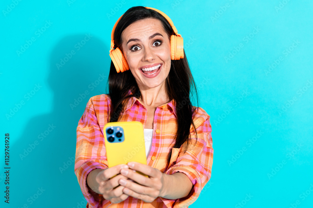 Photo of pretty young girl headphones hold device excited wear trendy plaid outfit isolated on aquamarine color background Photo of pretty young girl headphones hold device excited wear trendy plaid outfit isolated on aquamarine color background