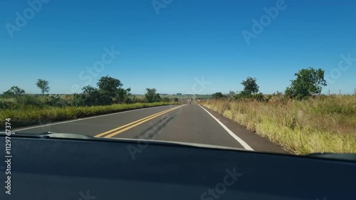 Car on a highway driving fast with fields, green areas and farms around on a blue sky day. Driving on a highway of Brazil.