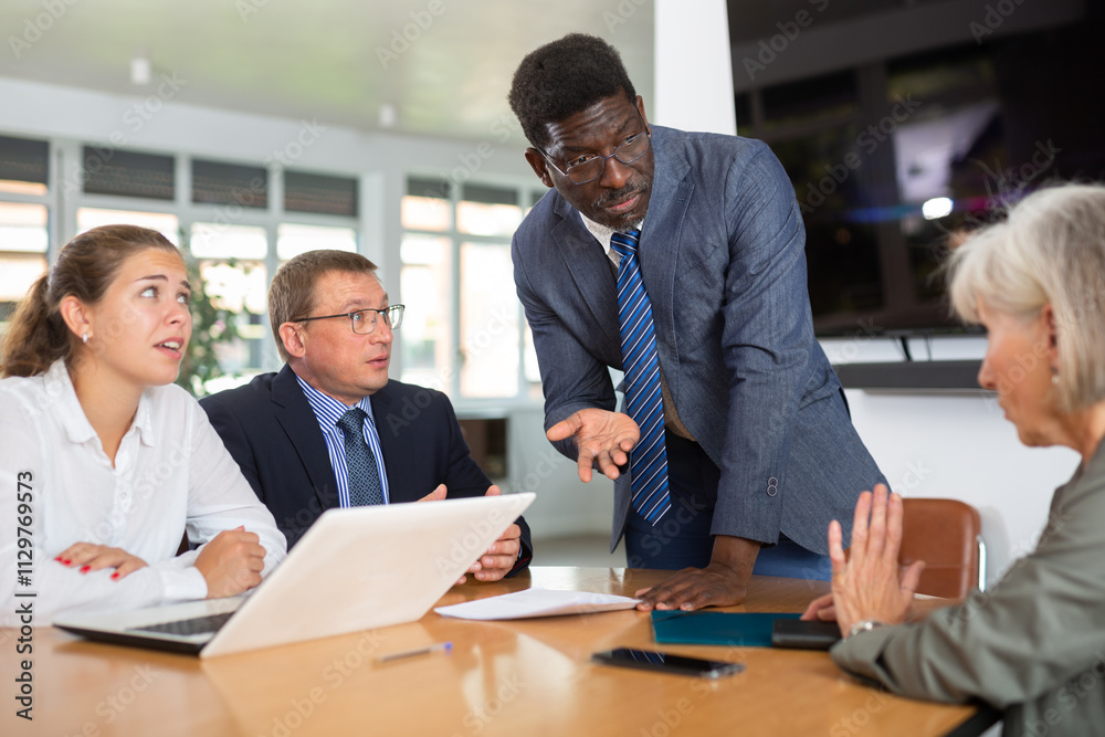 Group of different business people arguing while discussing work issues at table in office Group of different business people arguing while discussing work issues at table in office