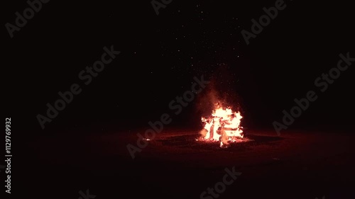 Bonfire made of logs burning with hot flames, with sparks flying. Bonfire isolated in the darkness, aligned to the right.