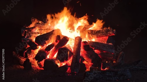 Bonfire made of logs burning with hot flames, with sparks flying. Bonfire isolated in the darkness. 