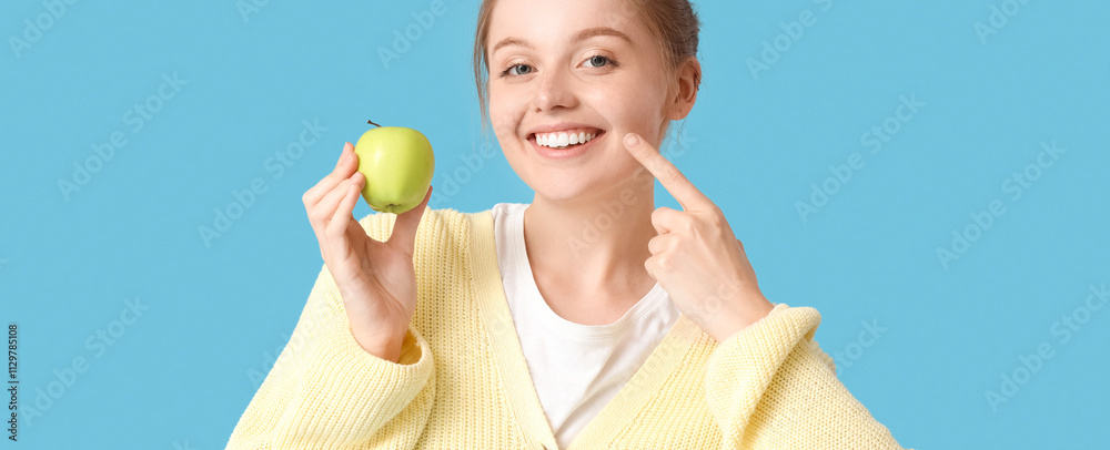Young woman with green apple pointing at her teeth on blue background Young woman with green apple pointing at her teeth on blue background