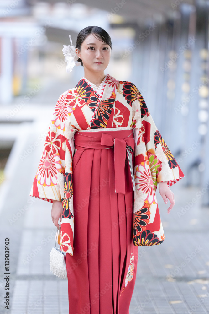 A Japanese woman in her 20s wearing a red hakama, a staple for Japanese university graduates, stands in front of a cultural building.