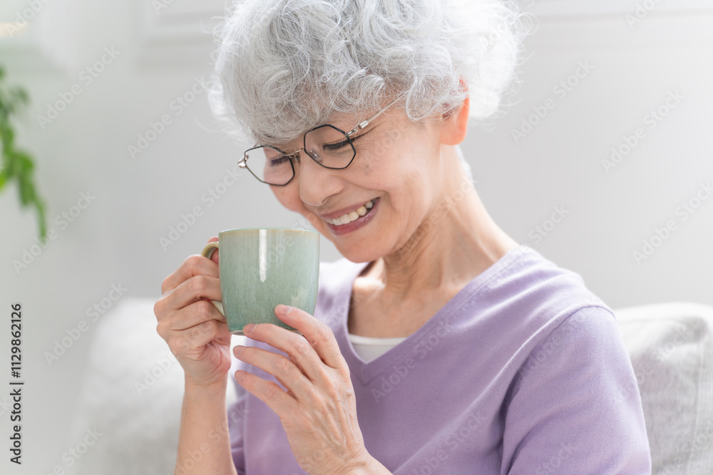 ソファーでコーヒーを飲みながらくつろぐシニア女性 ソファーでコーヒーを飲みながらくつろぐシニア女性