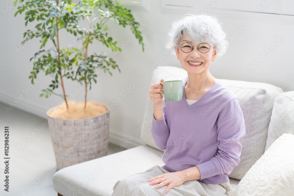 ソファーでコーヒーを飲みながらくつろぐシニア女性 ソファーでコーヒーを飲みながらくつろぐシニア女性
