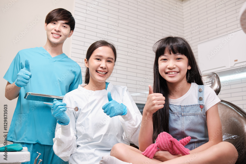 Portrait of Asian female pediatric dentist, assistant, and a girl patient smiling and looking at camera in dental clinic, mouth hygiene, and professional orthodontic healthcare work in a kid hospital. Portrait of Asian female pediatric dentist, assistant, and a girl patient smiling and looking at camera in dental clinic, mouth hygiene, and professional orthodontic healthcare work in a kid hospital.