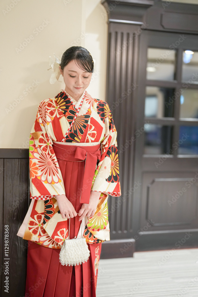 Fototapeta premium A Japanese woman in her 20s stands in front of an interior door wearing a red kimono (hakama), a staple of Japanese university graduates.