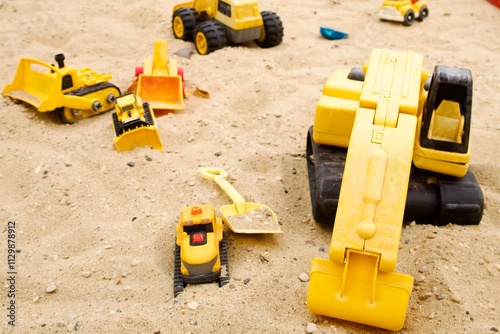 yellow toy excavators and trucks on sand in a childrens sandbox