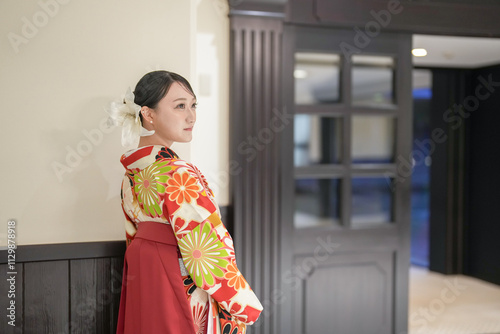 A Japanese woman in her 20s stands in front of an interior door wearing a red kimono (hakama), a staple of Japanese university graduates. photo