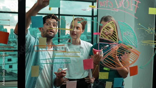 Group of professional business team working together, discussing and writing at sticky notes about marketing idea,plan, strategy at glass wall with graph and colorful sticky notes. Tracery