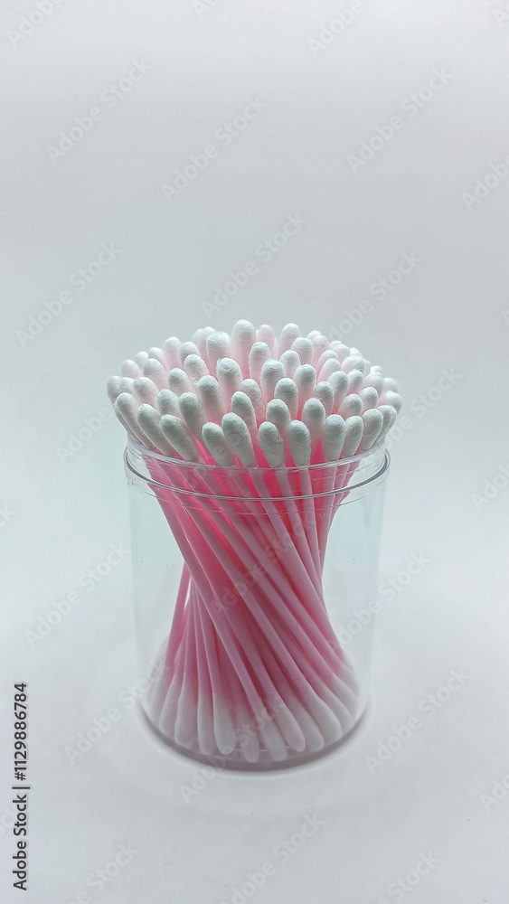A container of pink-handled cotton swabs neatly arranged in a transparent plastic jar on a white backdrop. A container of pink-handled cotton swabs neatly arranged in a transparent plastic jar on a white backdrop.