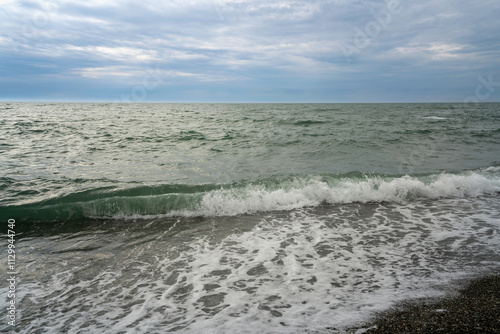 An incoming wave on the Black Sea and a pebble beach on the Sochi coast on a summer day with clouds, Sochi, Krasnodar Territory, Russia photo