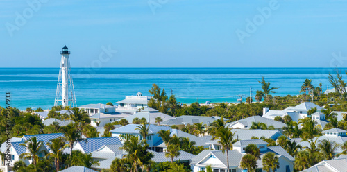 Fototapeta Naklejka Na Ścianę i Meble -  Expensive mansions between green palm trees in island small town Boca Grande in southwest Florida, USA. White lighthouse on sea shore for commercial vessels navigation