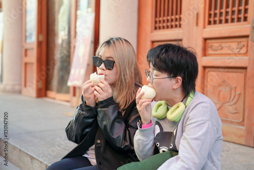 Two Chinese women in their 30s eating steamed buns in front of historical building in Jing'an District, Shanghai, China photo