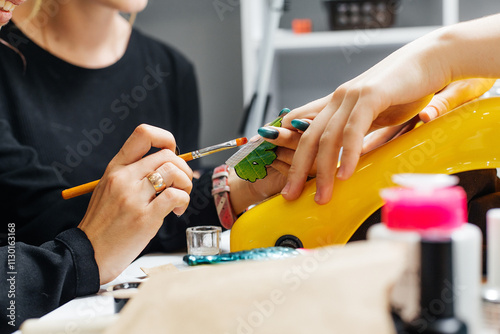 manicure process. a woman in black clothes holds a brush and applies something to the nail of her other hand. The nail has an extension mold that looks like a green leaf. photo