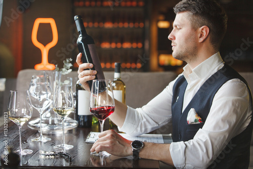 Wine steward holds wineglass, bottle of red beverage.