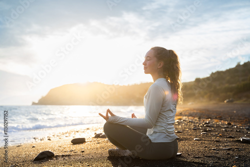 Side view of a young adult woman meditating in lotus yoga pose. A calm female yogi practices yoga and meditations among the sea and mountains at the sunset. Do yoga and spiritual practice outdoors. photo