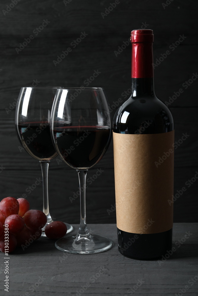 Fototapeta premium Bottle of red wine with grapes, corkscrew and corks on wooden background