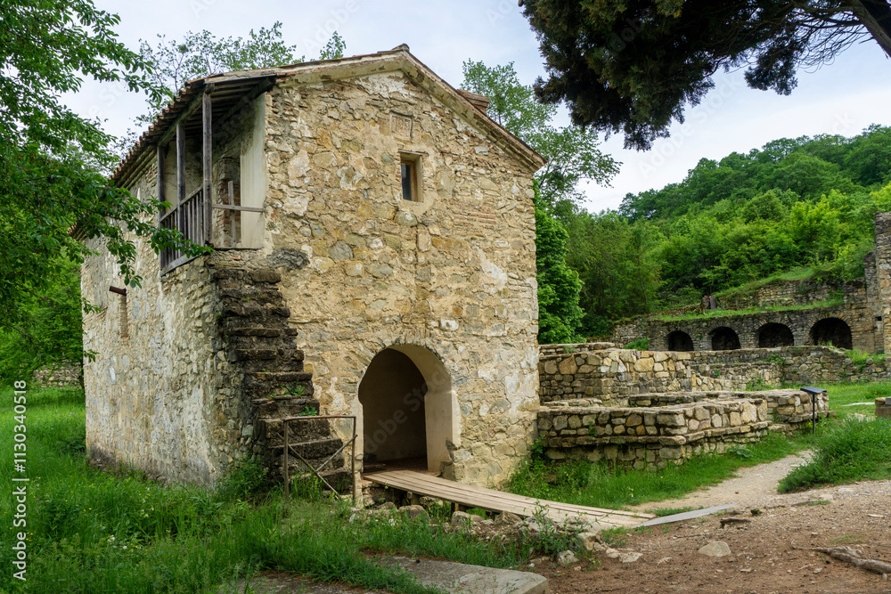Obraz premium A small church on the grounds of Ikalto Academy. Stone walls and stairs, arched entrance. Green grass, sky with clouds.