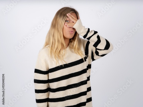 Beautiful teen girl wearing striped sweater peeking in shock covering face and eyes with hand, looking through fingers with embarrassed expression. photo